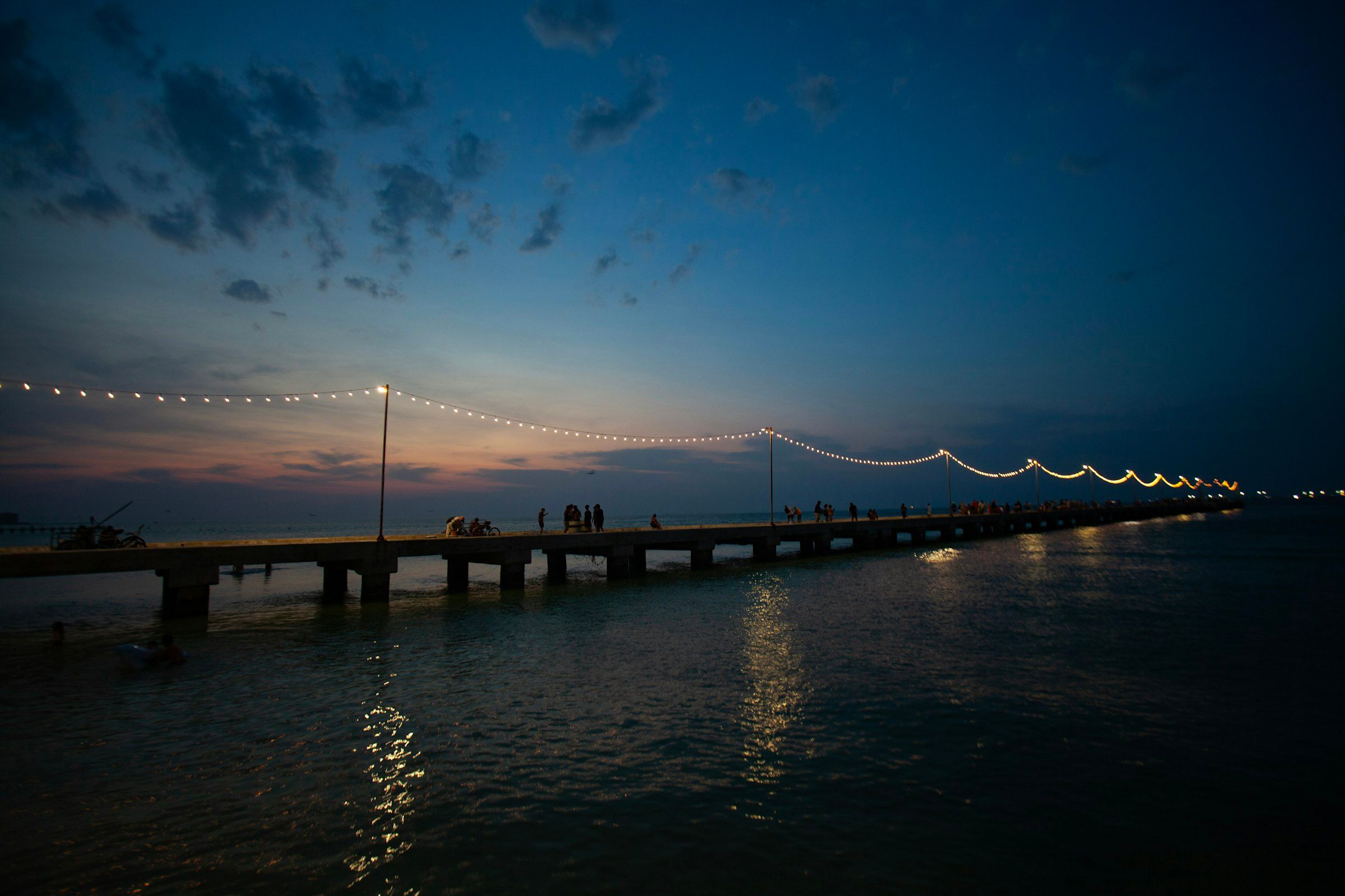 Un lungo pontile illuminato sul mare calmo dopo il tramonto, con alcune persone in fondo: col buio le luci dei moli attirano i pesciolini e i calamari che li cacciano.