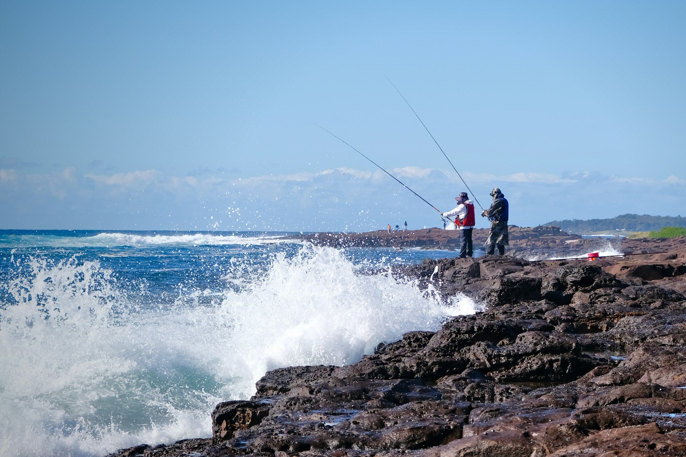 Due pescatori con le canne sulla scogliera mentre le onde si frangono poco più in là: il mare mosso che cerca chi fa spinning alla spigola.